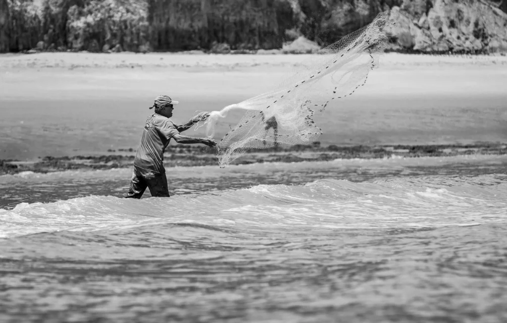 Traditional fishing practice: a man throwing fishing net in the ocean tides.