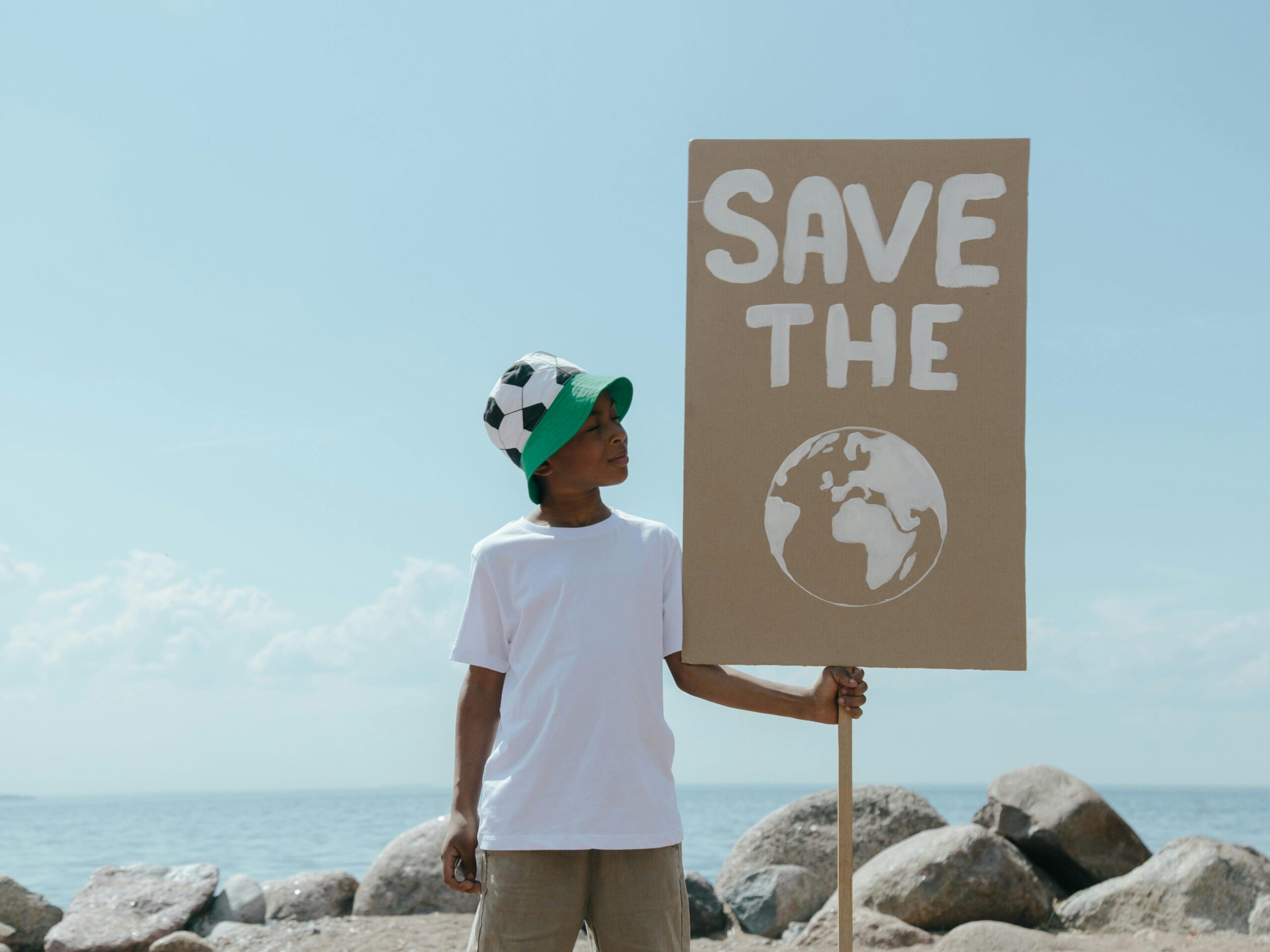 Young boy at beach holding a sign promoting environmental awareness and earth conservation.