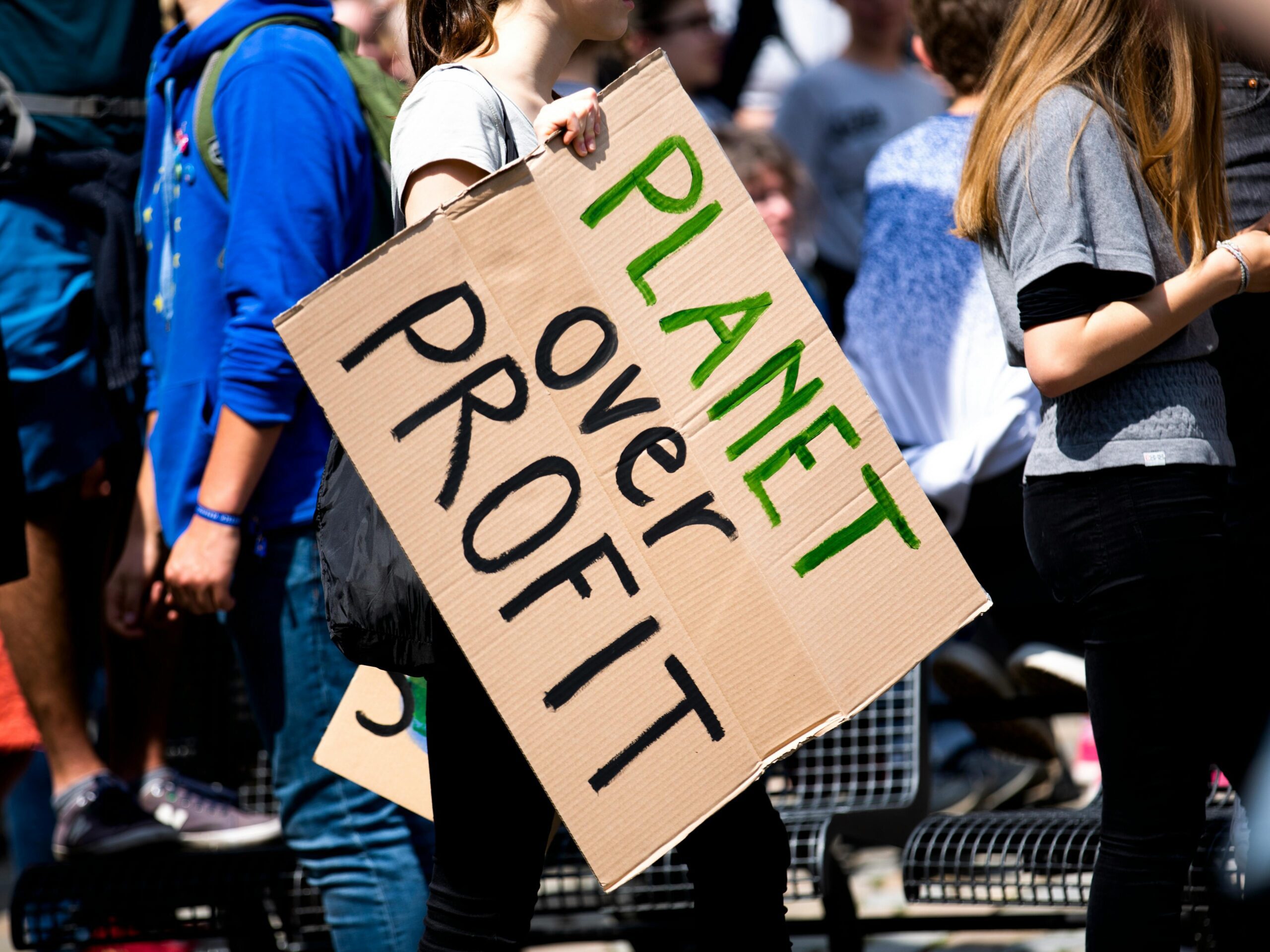 Youth climate protest with participants holding 'Planet Over Profit' sign.