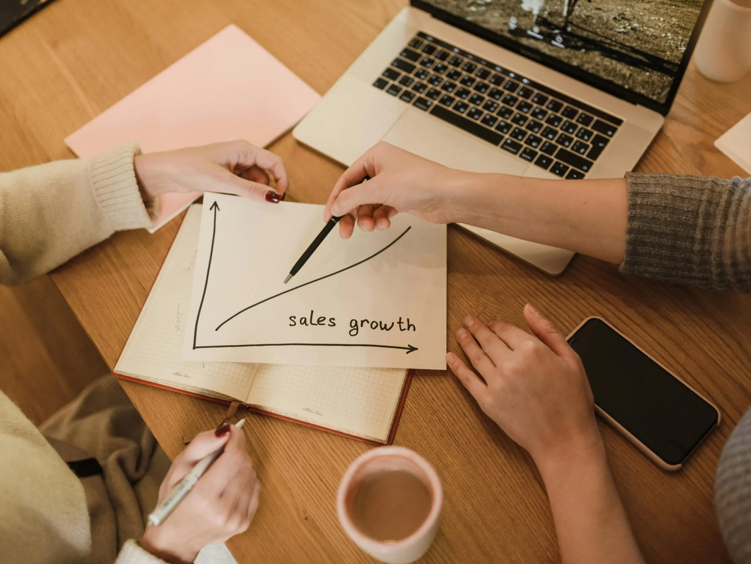 Two women plan sales growth with graphs and technology in an office setting.