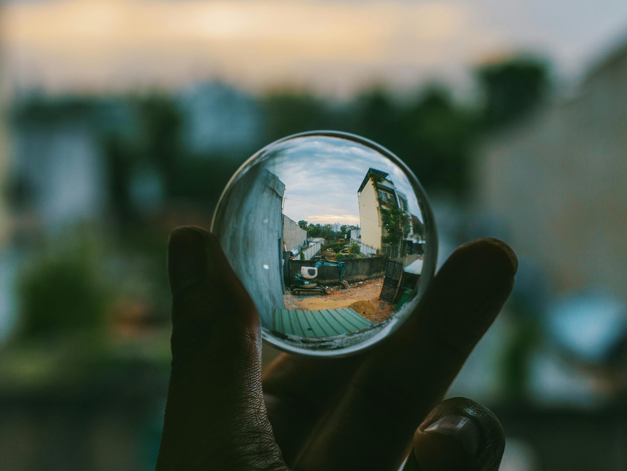 A hand holding a crystal ball reflecting an urban street scene outdoors.